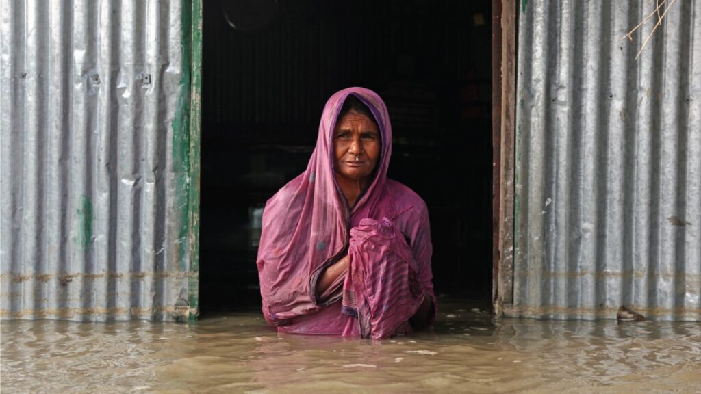 Elderly woman standing at her doorstep, chest-deep in floodwater.